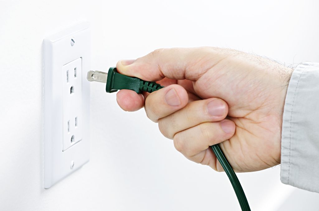 Man plugging a Christmas light power cord into an electrical outlet
